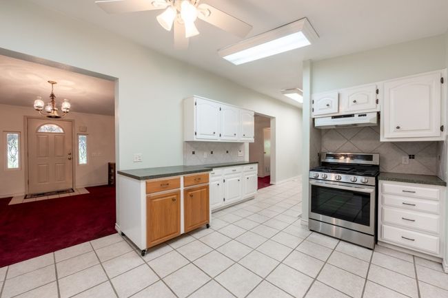 Kitchen featuring stainless steel gas stove, under cabinet range hood, dark countertops, a chandelier, and light tile patterned floors | Image 18