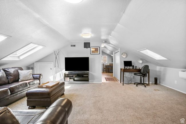 Carpeted living area featuring vaulted ceiling with skylight, visible vents, and baseboards | Image 16