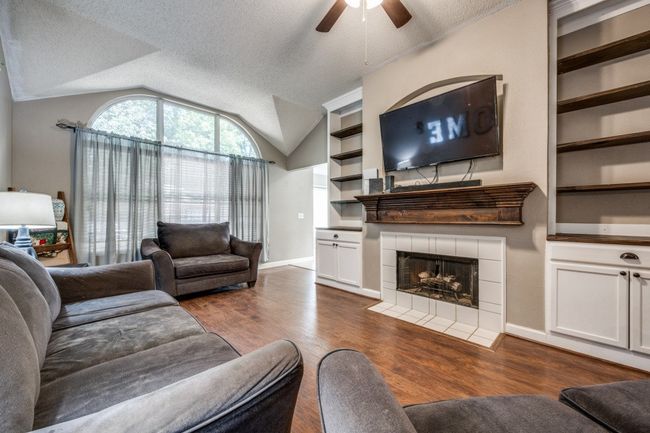 Living room featuring a ceiling fan, lofted ceiling, dark wood-type flooring, a fireplace, and a textured ceiling | Image 6