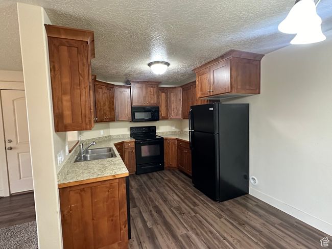 Kitchen with a textured ceiling, dark wood-style flooring, a sink, light countertops, and black appliances | Image 8