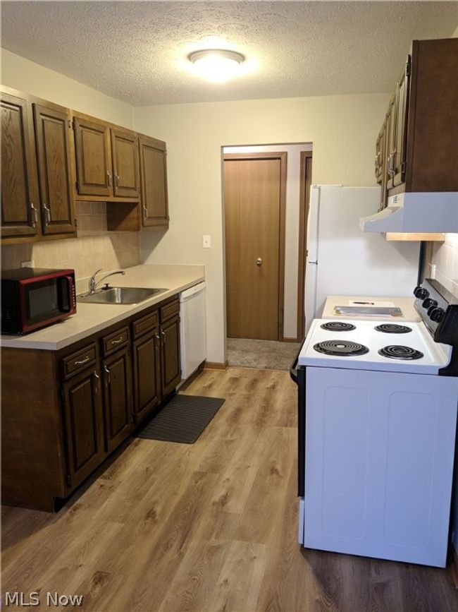 Kitchen with range hood, light hardwood / wood-style flooring, white appliances, backsplash, and sink | Image 12