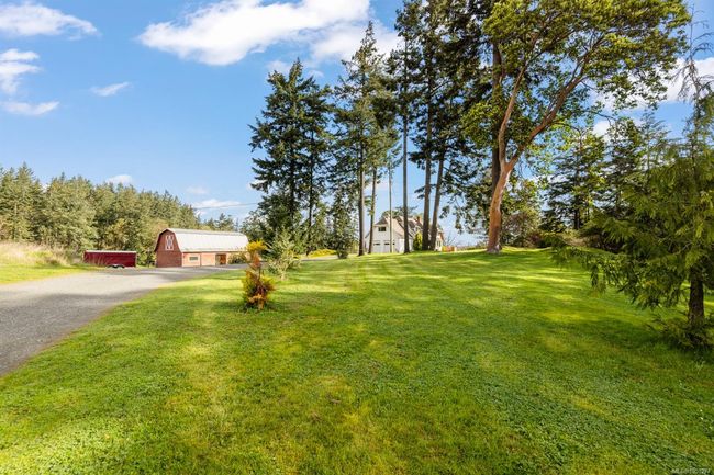 View of grassy yard with a detached garage, gravel driveway, and an outdoor structure | Image 47