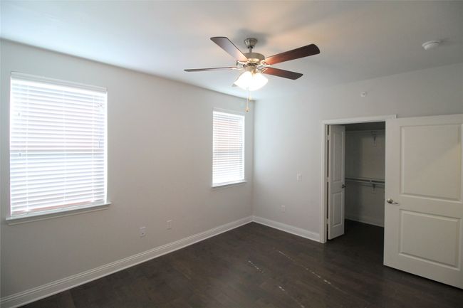 Unfurnished bedroom featuring a walk in closet, a closet, baseboards, ceiling fan, and dark wood-style flooring | Image 5