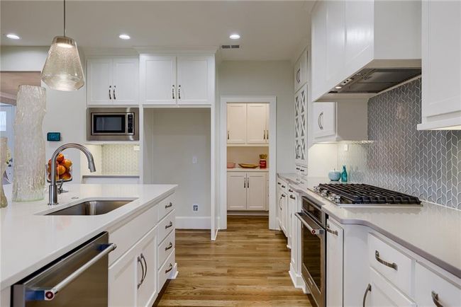 Kitchen with appliances with stainless steel finishes, custom exhaust hood, sink, backsplash, and light hardwood / wood-style flooring | Image 18