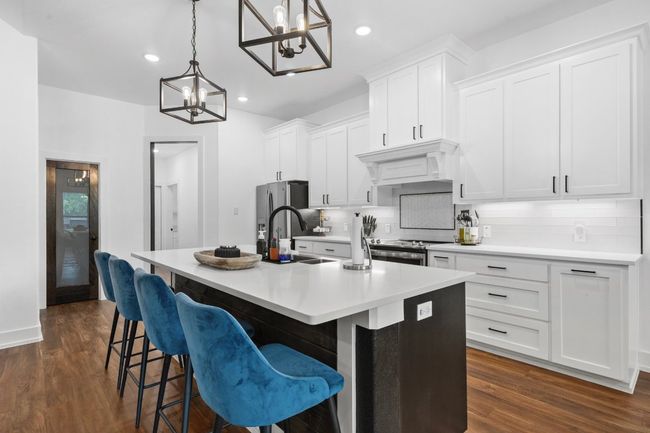 Kitchen with custom exhaust hood, a sink, a chandelier, a center island with sink, and decorative backsplash | Image 10