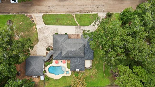 This aerial view shows a spacious home with a well-maintained yard, a large driveway, and a backyard featuring a pool and patio area surrounded by mature trees, offering privacy and a serene atmosphere. | Image 4