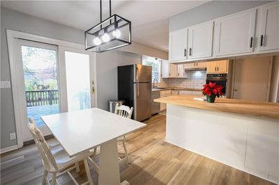 Kitchen featuring a healthy amount of sunlight, butcher block countertops, decorative light fixtures, white cabinets, and appliances with stainless steel finishes | Image 3