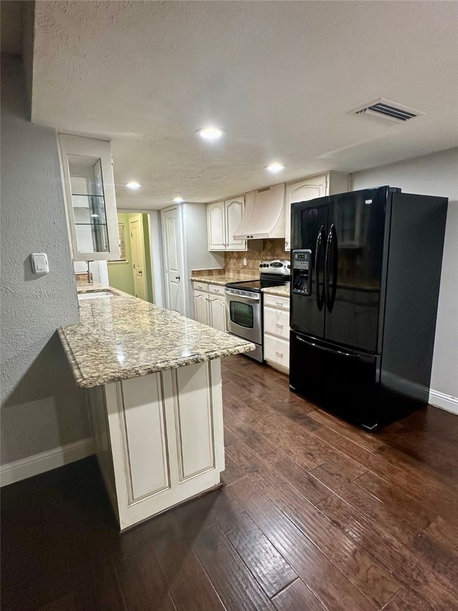 Kitchen with black fridge, a peninsula, stainless steel electric range oven, tasteful backsplash, and light stone counters | Image 13