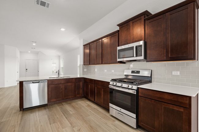 Kitchen with appliances with stainless steel finishes, a sink, light wood finished floors, decorative backsplash, and recessed lighting | Image 10