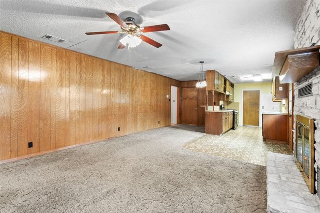 Unfurnished living room featuring a glass covered fireplace, ceiling fan, wood walls, light colored carpet, and a textured ceiling | Image 17