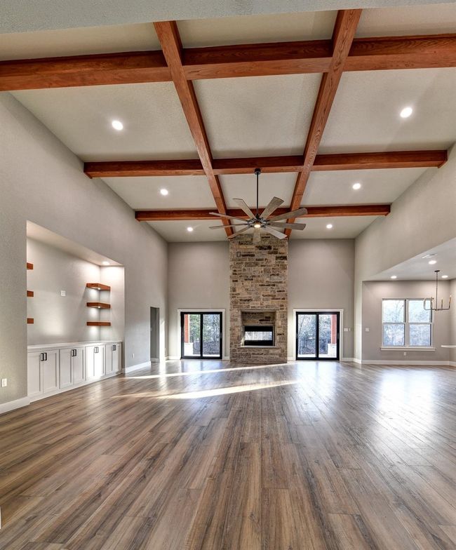 Unfurnished living room with beam ceiling, ceiling fan, coffered ceiling, a stone fireplace, and hardwood / wood-style floors | Image 16