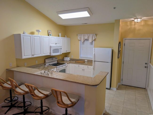 Kitchen featuring a peninsula, white appliances, a kitchen bar, white cabinetry, and light tile patterned floors | Image 6