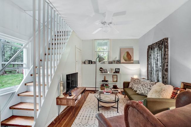 Living area with stairway, a baseboard heating unit, a ceiling fan, and wood finished floors | Image 6