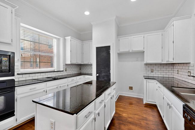 Kitchen with backsplash, a center island, white cabinetry, dark wood-style flooring, and ornamental molding | Image 16