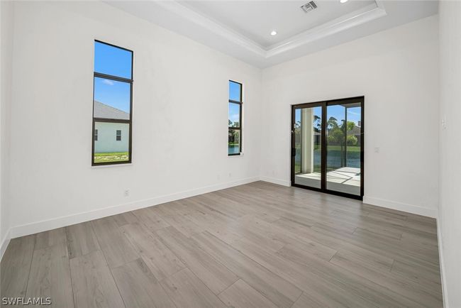 13'-0" x 17'-7" Master bedroom with 13' ceiling, designer wind rated windows and slider to Lanai and pool with a serene water view. | Image 9