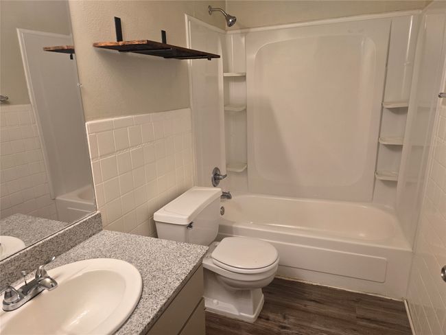 Bathroom featuring tile walls, wood finished floors, tub / shower combination, vanity, and a wainscoted wall | Image 11