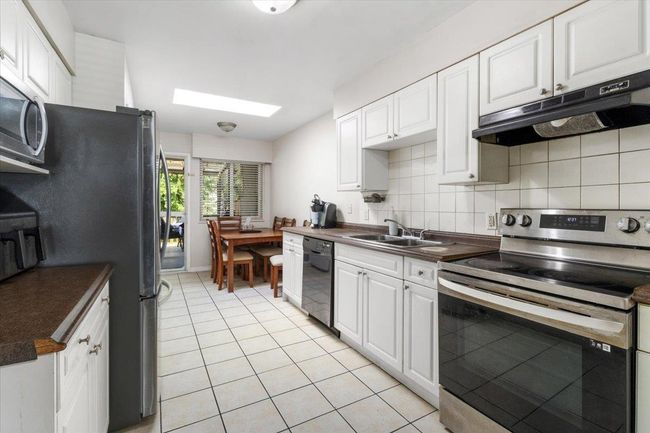 Kitchen featuring under cabinet range hood, a sink, dark countertops, stainless steel appliances, and a skylight | Image 11