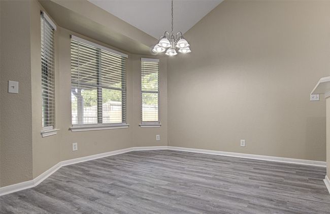 Empty room with a chandelier, wood finished floors, and lofted ceiling | Image 6