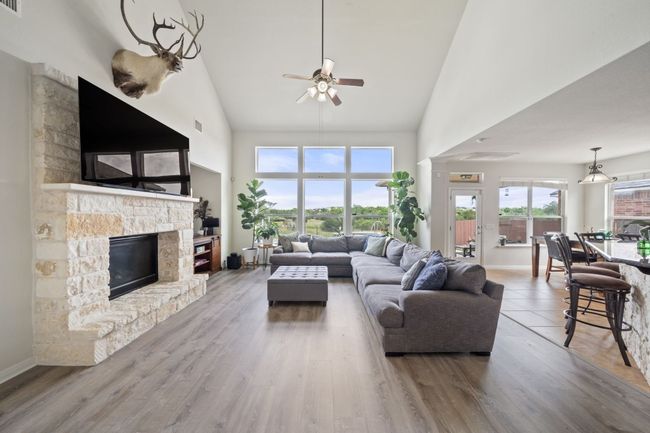 Living area with high vaulted ceiling, ceiling fan, a stone fireplace, and wood finished floors | Image 4