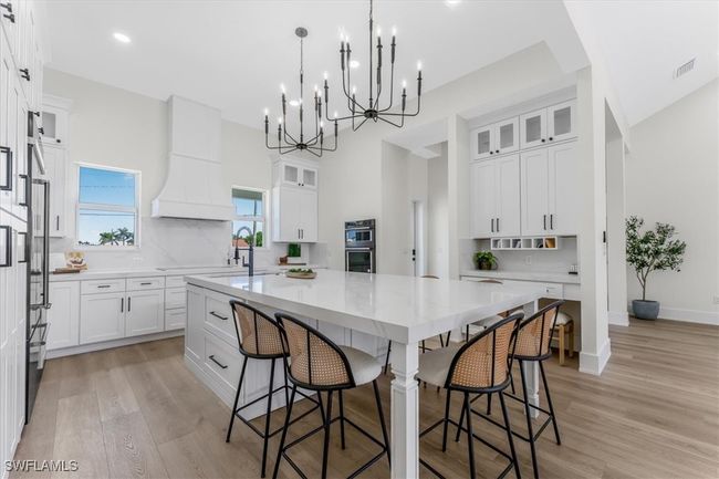 Kitchen with a spacious island, white cabinets, a kitchen breakfast bar, light wood finished floors, and recessed lighting | Image 6