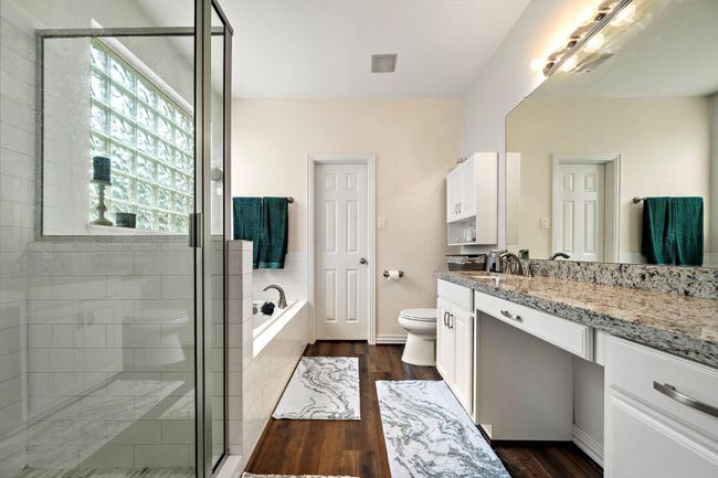 This spacious bathroom features a modern glass-enclosed shower, a luxurious soaking tub, and a long granite vanity with ample storage. The large window provides natural light. Master bedroom also has a large walk-in closet with built in storage. | Image 12