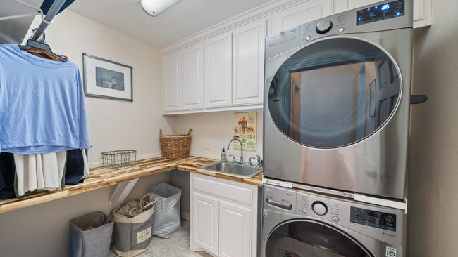 Laundry area featuring cabinet space, a sink, and stacked washing maching and dryer | Image 30