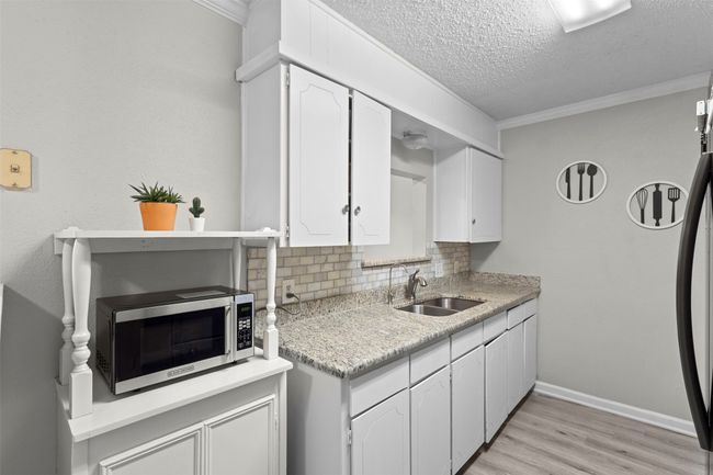 Kitchen with light wood-type flooring, a sink, stainless steel microwave, and white cabinets | Image 16