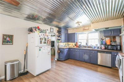 Kitchen featuring backsplash, light hardwood / wood-style floors, sink, white appliances, and blue cabinets | Image 3