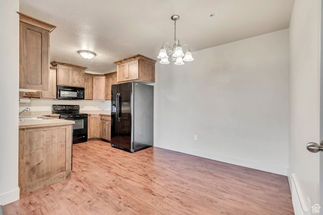 Kitchen featuring black appliances, light countertops, light wood-style flooring, pendant lighting, and a chandelier | Image 7