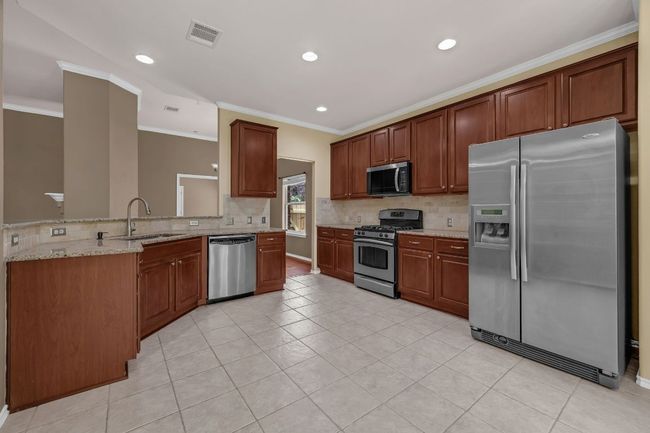 . The open-concept kitchen is a chef’s dream, offering granite countertops, stainless steel appliances, recessed lighting, cherry cabinetry with pull-out shelves, and a convenient breakfast bar overlooking the living room. | Image 9