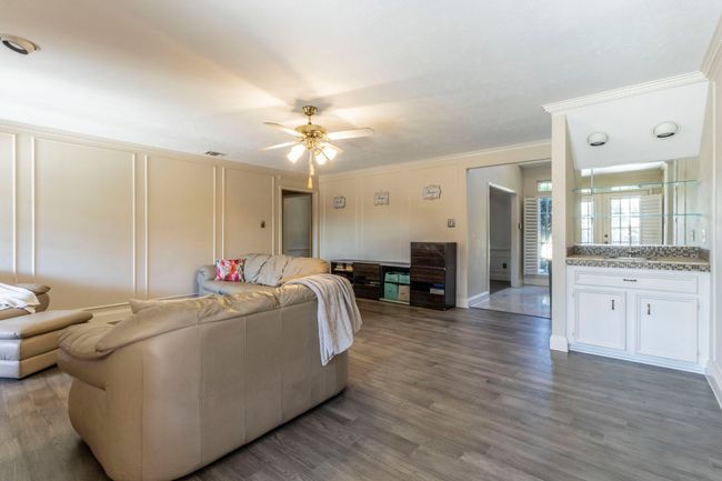 Living area with crown molding, ceiling fan, dark wood-style floors, and a decorative wall | Image 4