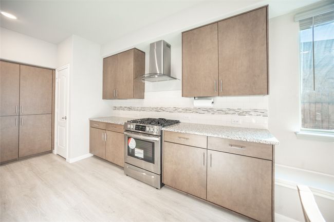 Kitchen with backsplash, wall chimney range hood, gas stove, and light hardwood / wood-style flooring | Image 9