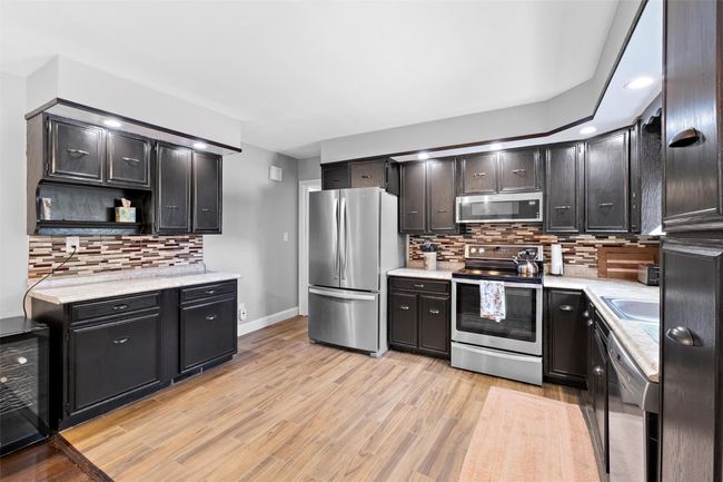 Kitchen with open shelves, stainless steel appliances, light countertops, light wood-style floors, and beverage cooler | Image 14