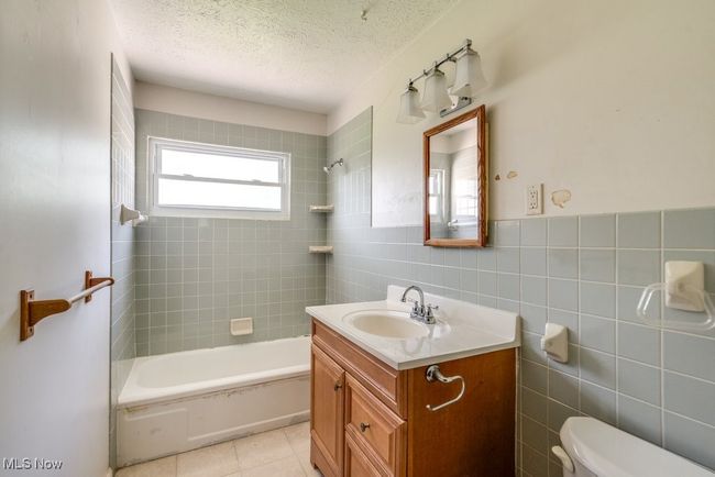 Full bathroom with vanity, tile walls, toilet, shower / washtub combination, and a textured ceiling | Image 22