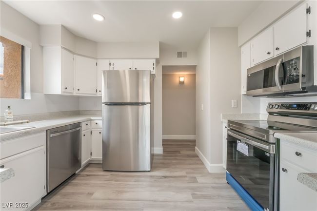Kitchen with stainless steel appliances, white cabinetry, light countertops, recessed lighting, and light wood-style floors | Image 9