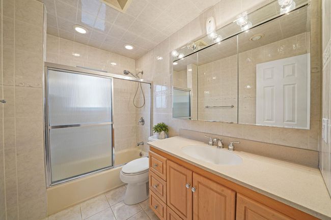 Full bathroom with toilet, tile patterned flooring, tile walls, shower / bath combination with glass door, and vanity | Image 14