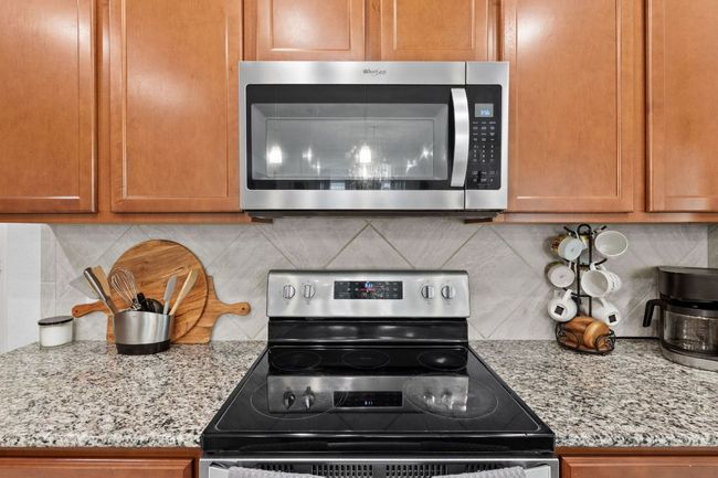 Kitchen with stainless steel appliances, backsplash, brown cabinetry, and light stone counters | Image 11