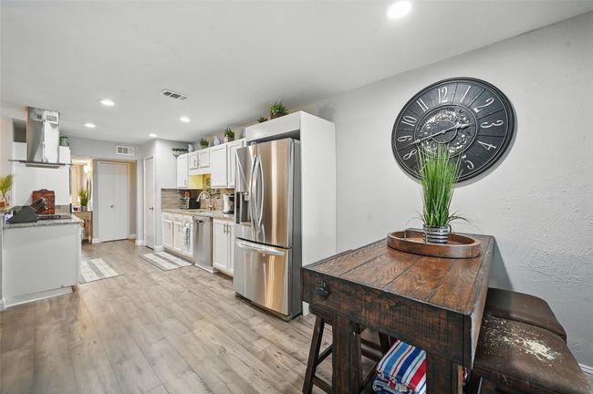 Kitchen with stainless steel appliances, exhaust hood, white cabinets, light wood finished floors, and recessed lighting | Image 17