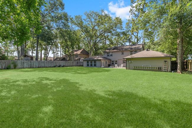 Spacious backyard with lush green lawn, mature trees, and a large two-story house featuring a patio. | Image 36