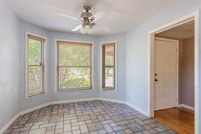 Unfurnished room with healthy amount of natural light, a ceiling fan, light stone finish floors, and a textured ceiling | Image 6
