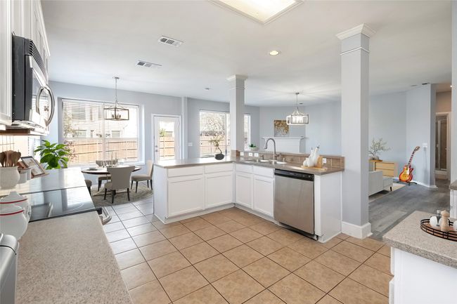 Kitchen featuring stainless steel appliances, white cabinets, hanging light fixtures, and ornate columns | Image 4