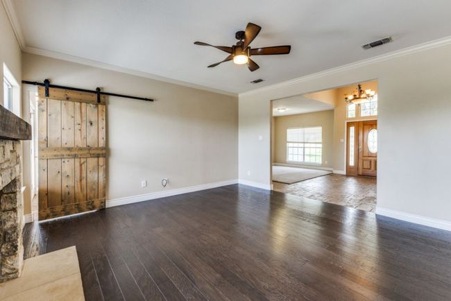 Unfurnished living room featuring crown molding, visible vents, and ceiling fan with notable chandelier | Image 6