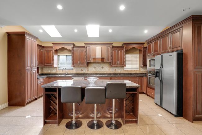 Kitchen featuring stainless steel appliances, decorative backsplash, wall chimney exhaust hood, a breakfast bar area, and a kitchen island | Image 16