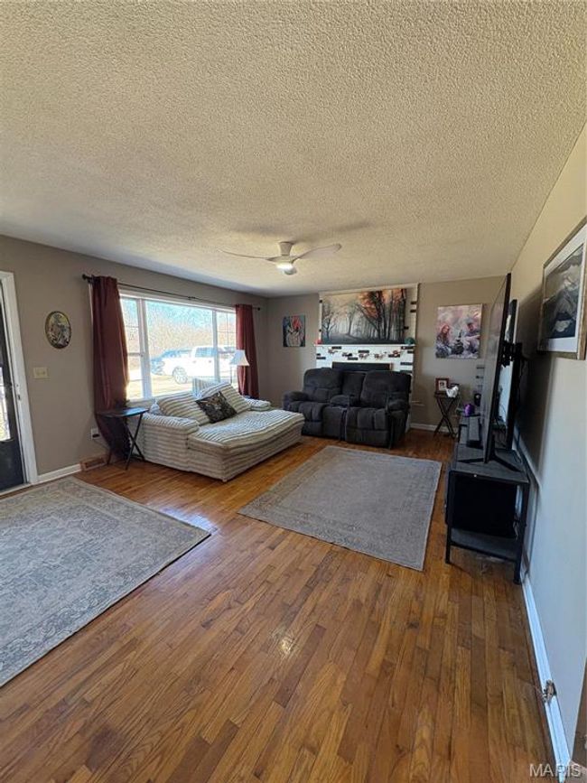 Living area featuring a textured ceiling, ceiling fan, wood-type flooring, and baseboards | Image 9