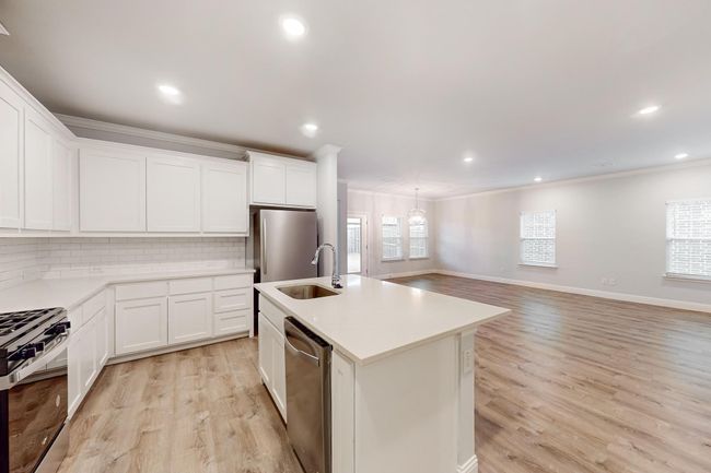 Kitchen with appliances with stainless steel finishes, white cabinetry, an island with sink, sink, and crown molding | Image 7