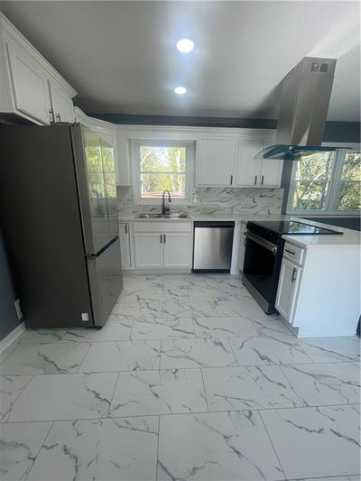 Kitchen featuring white cabinets, extractor fan, dishwashing machine, fridge, and range | Image 3