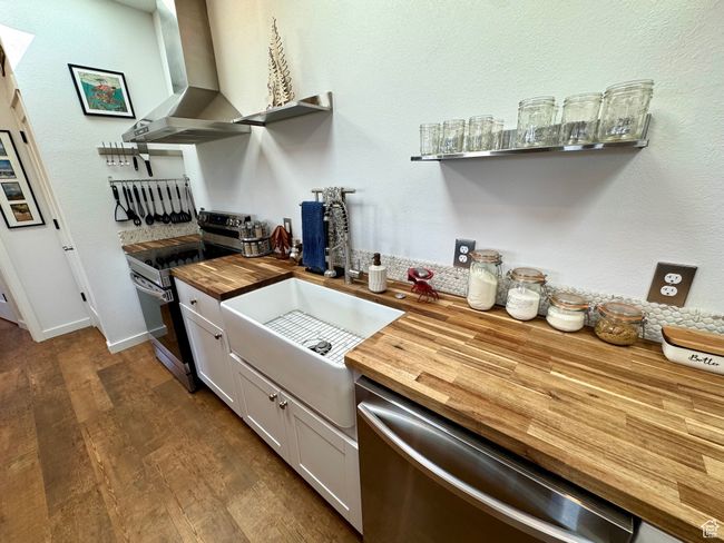 Kitchen with butcher block countertops, appliances with stainless steel finishes, a farmhouse sink, exhaust hood, and wood-style floors | Image 7