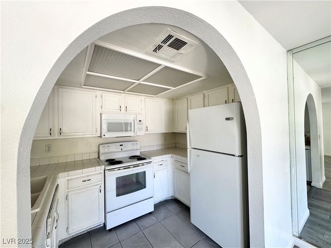 Kitchen with white appliances, white cabinets, tile counters, cooling unit, and dark tile patterned flooring | Image 7