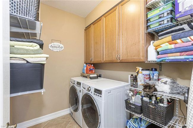 Laundry area featuring light tile patterned floors, baseboards, cabinet space, and washer and clothes dryer | Image 21