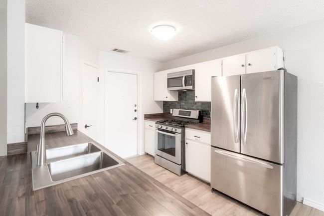 Kitchen featuring stainless steel appliances, white cabinetry, light wood finished floors, decorative backsplash, and dark countertops | Image 12